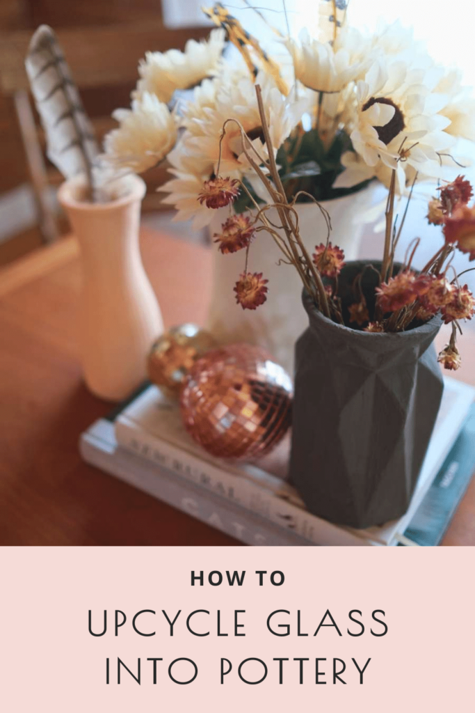 Gray, white, and pink vases filled with dried flowers and feathers sit beside two copper disco balls atop two books on a dining room table. Text reads "how to upcycle glass into pottery."