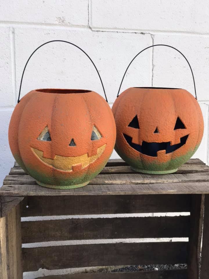 Budget-friendly DIY Halloween decor: Two orange and green jack-o-lantern buckets sit atop a wooden table in front of a white wall. 