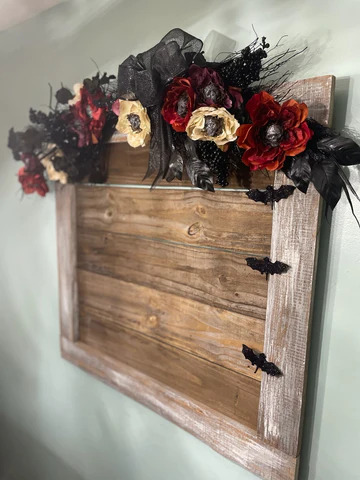Budget-friendly DIY Halloween decor: Wooden frame with black, red, and cream flowers adorned with glittery skulls and black bats. 